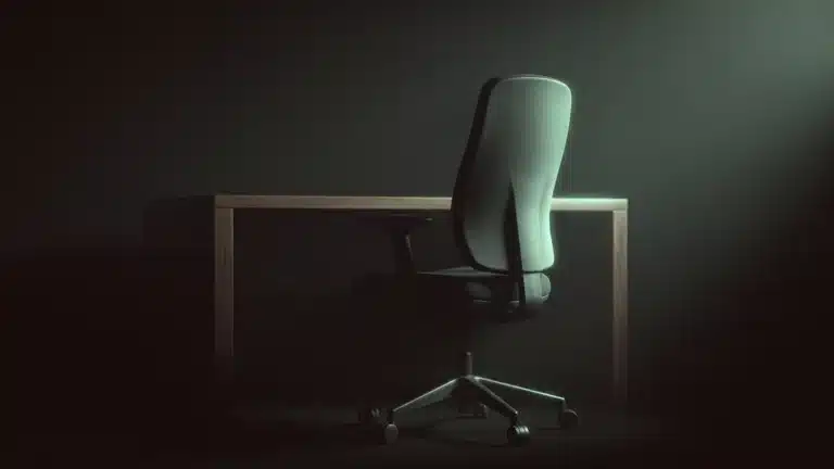 An empty office chair pulled up to a bare desk in a darkened room
