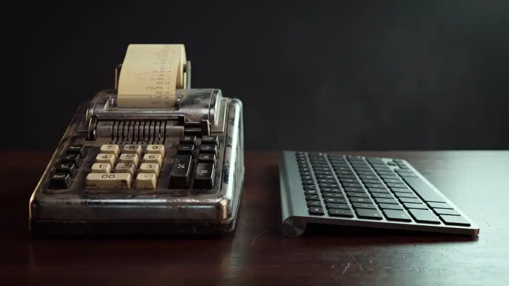 A vintage adding machine sitting beside a modern keyboard